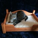 A black and gray tabby laying on a wooden cat bed.